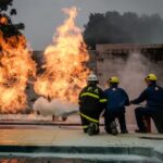 Firefighters in protective gear conduct a live fire training exercise outdoors.
